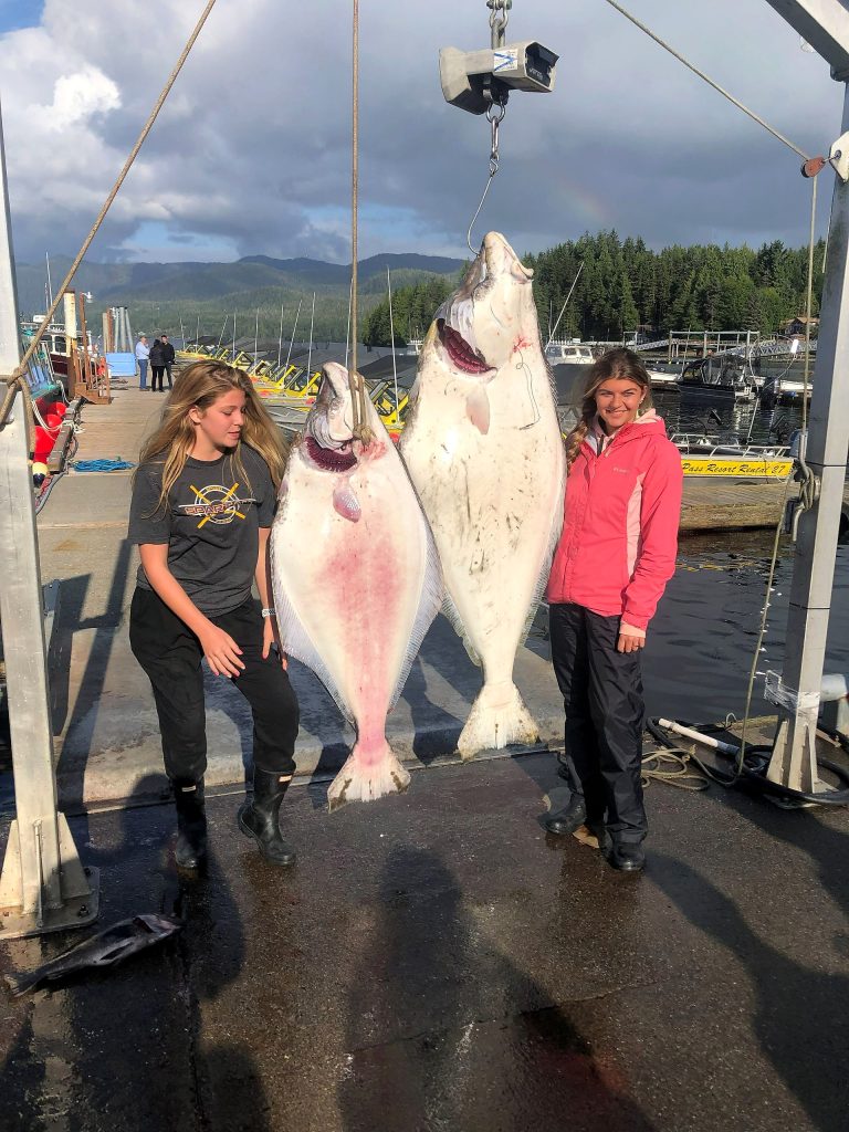 Two large halibut hanging at the dock with the guests who caught them