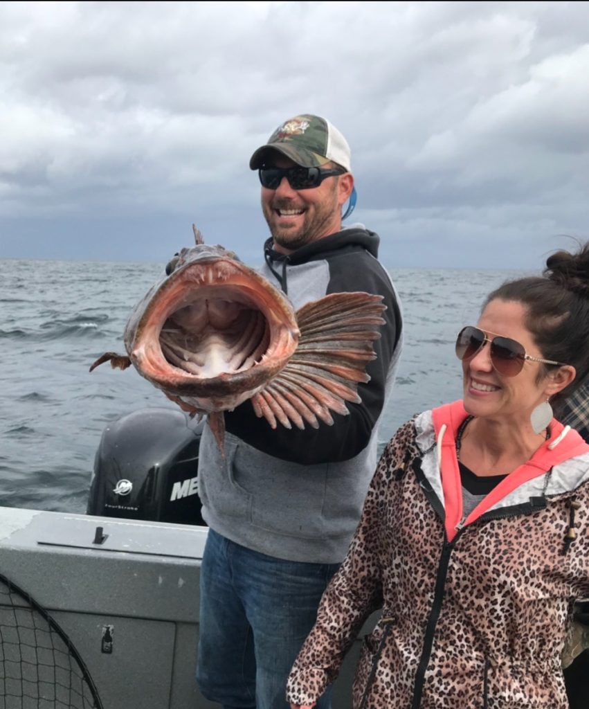 Couple holding a lingcod caught on their charter
