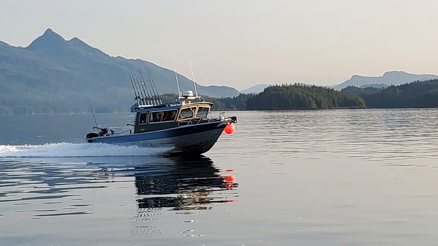 The Alaska Fishing Company charter boat running across calm water near Ketchikan with mountains behind