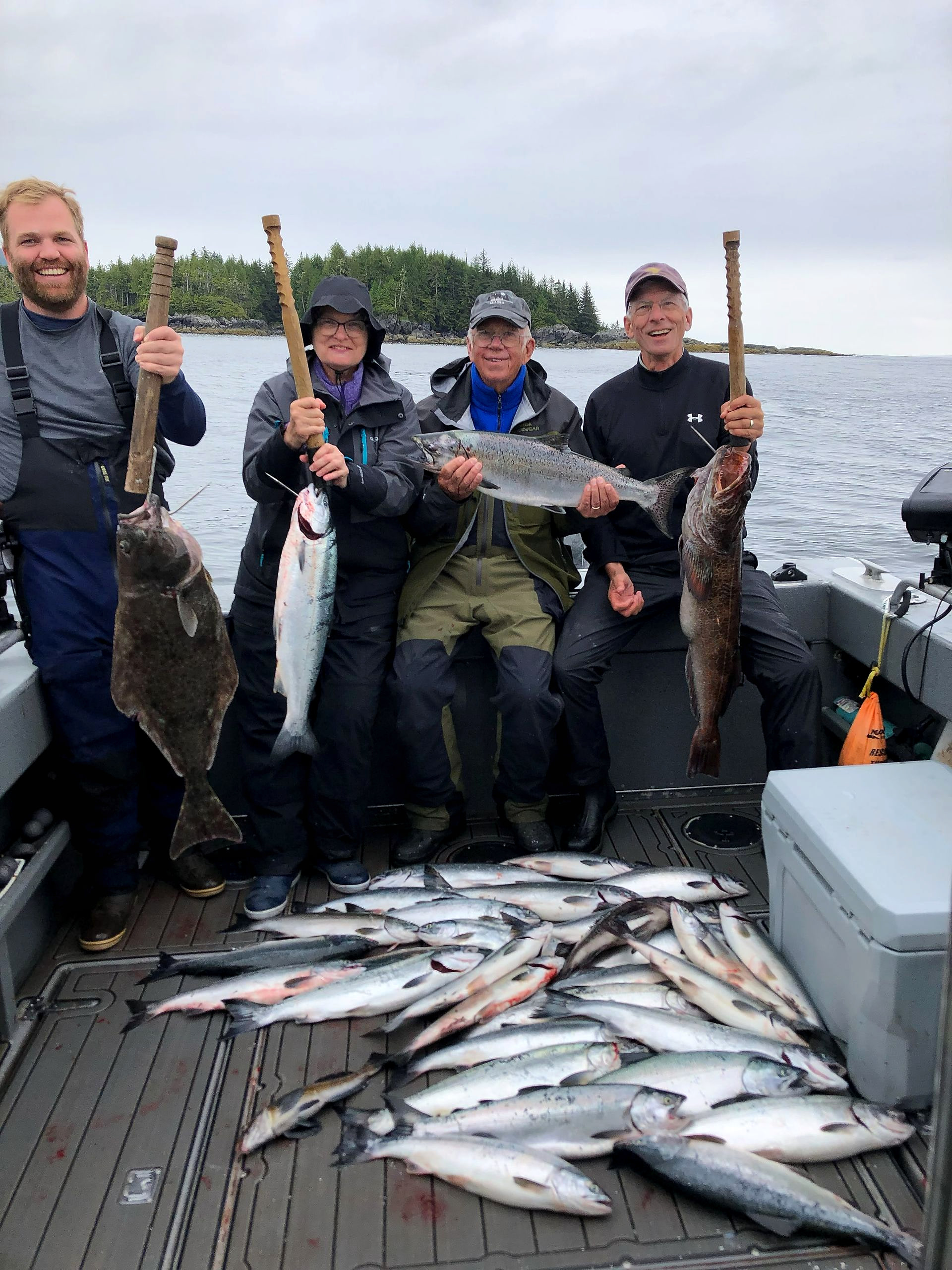 Four guests on the boat holding a halibut, salmon, and lingcod, with a deck full of salmon